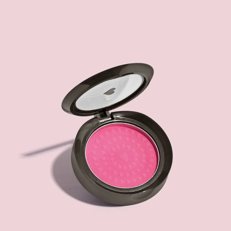 Estojo compacto redondo na cor preta com tampa transparente com coração ilustrado contendo 2g de blush em pó compacto Rubor Rosa Rosandilex da marca Quem Disse, Berenice? em fundo lilás.