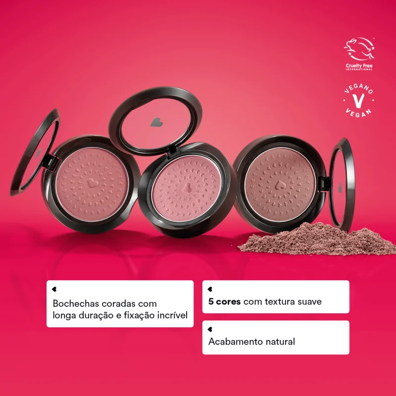 Três estojos compactos redondos pretos com tampas transparentes com coração ilustrado contendo, em cada um deles, 2g de blush em pó compacto da marca Quem Disse, Berenice? em fundo rosa vibrante e letras evidenciando os benefícios do produto.