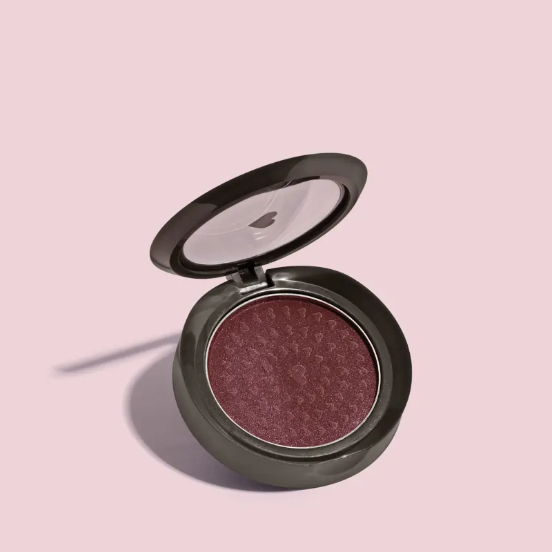 Estojo compacto redondo na cor preta com tampa transparente com coração ilustrado contendo 2g de blush em pó compacto Rubor Malva Amoratin da marca Quem Disse, Berenice? em fundo lilás.