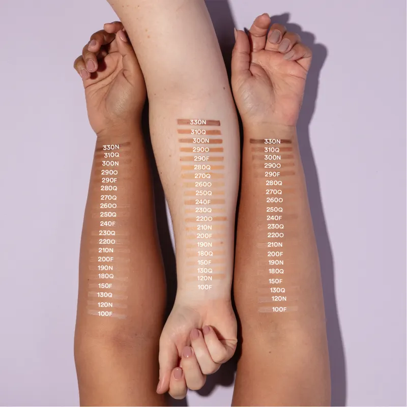 Imagem mostra três braços de cores diferentes estendidos sobre superfície branca sendo o braço mais a esquerda de pele negra, o do meio de pele branca e o da direita com pele parda, todos com diversos tons de base aplicados sobre eles e seus códigos.
