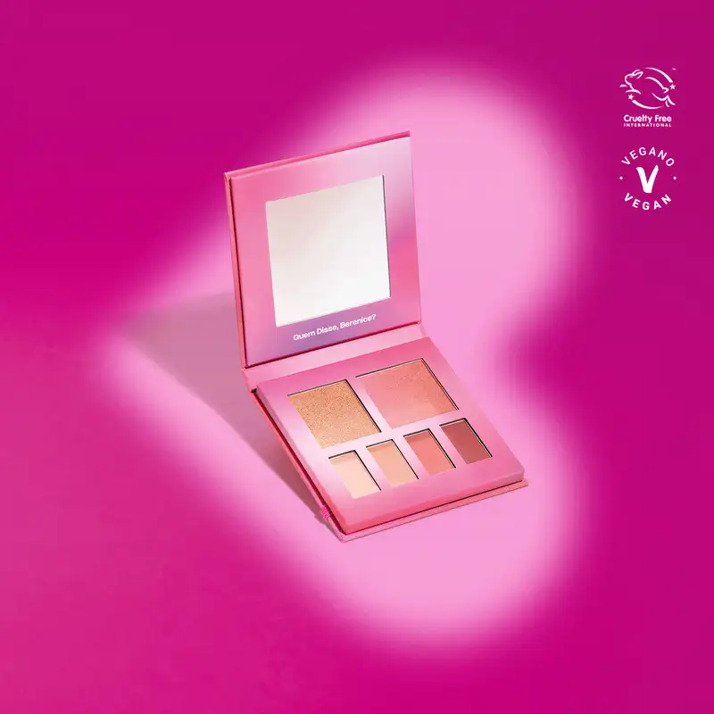 Paleta de maquiagem multifuncional Roselele Quem Disse, Berenice? em estojo na cor rosa com espelho na tampa contendo seis cores diferentes de sombras e blushes em tons de rosa em fundo roxo com sombras em volta do produto.