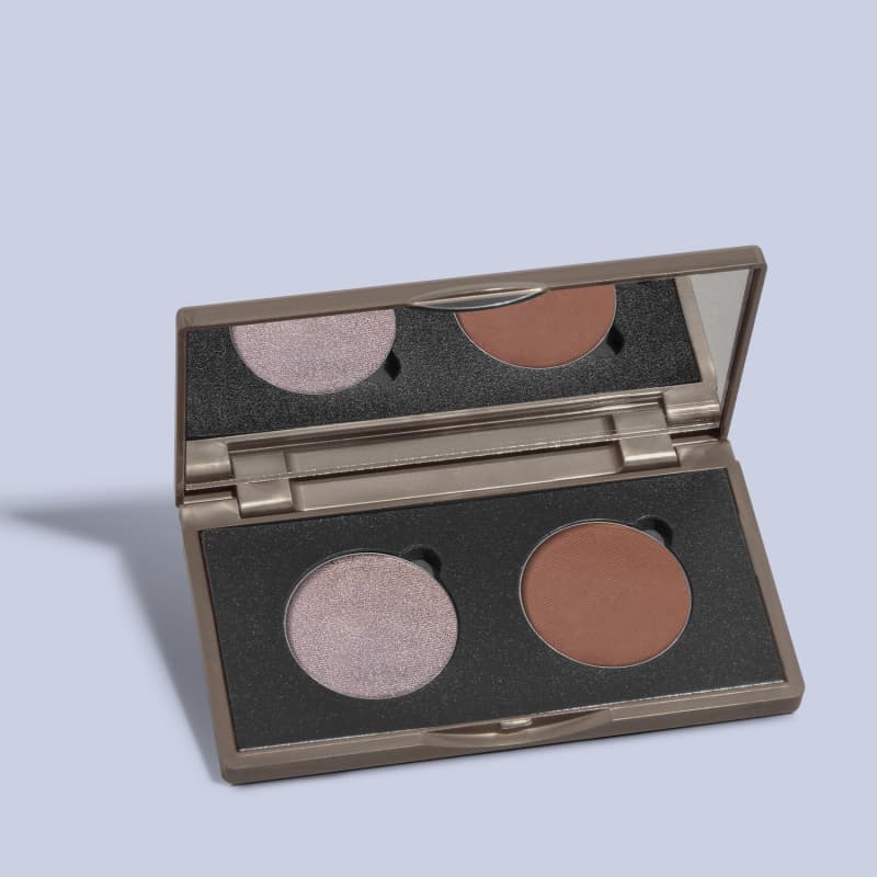 Paleta de sombras da marca Quem Disse, Berenice? com tom de prata e marrom em embalagem retangular preta e espelho na tampa em fundo azul claro com sombras.