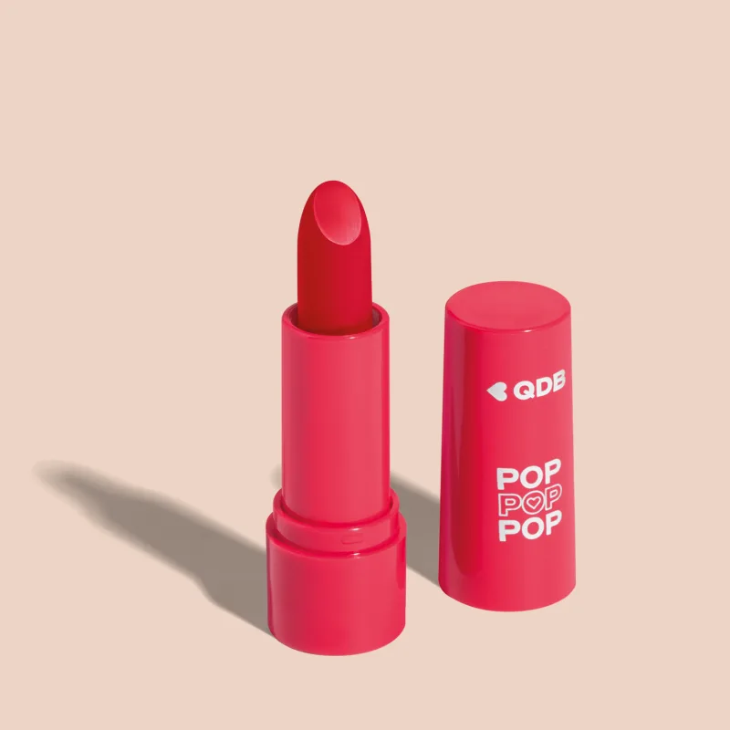 Imagem de um batom semi matte na cor Vermelho Icônico em embalagem rosa vibrante e tampa na mesma tonalidade com letras brancas. O produto faz parte da marca  POP Quem Disse, Berenice?. O fundo da imagem é lilás com sombreado.