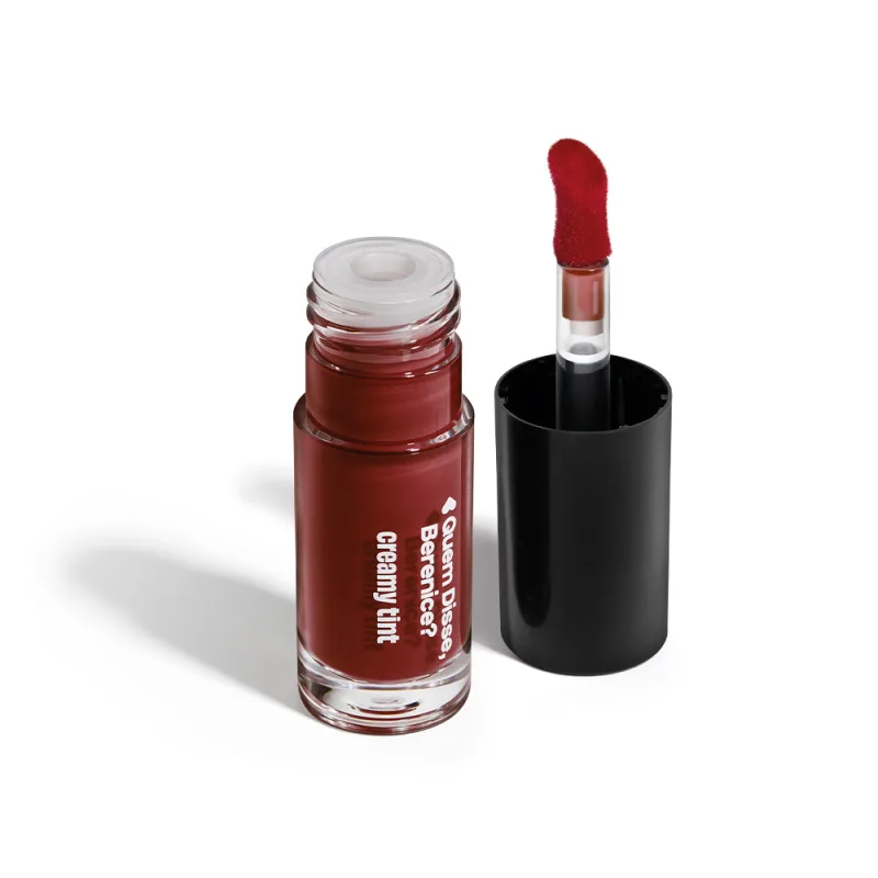 A imagem mostra um recipiente transparente de gloss labial da marca Quem Disse, Berenice? na cor vermelho cereja, com aplicador vermelho, haste transparente, tampa preta. Ele está em uma superfície branca com um leve sombreado.