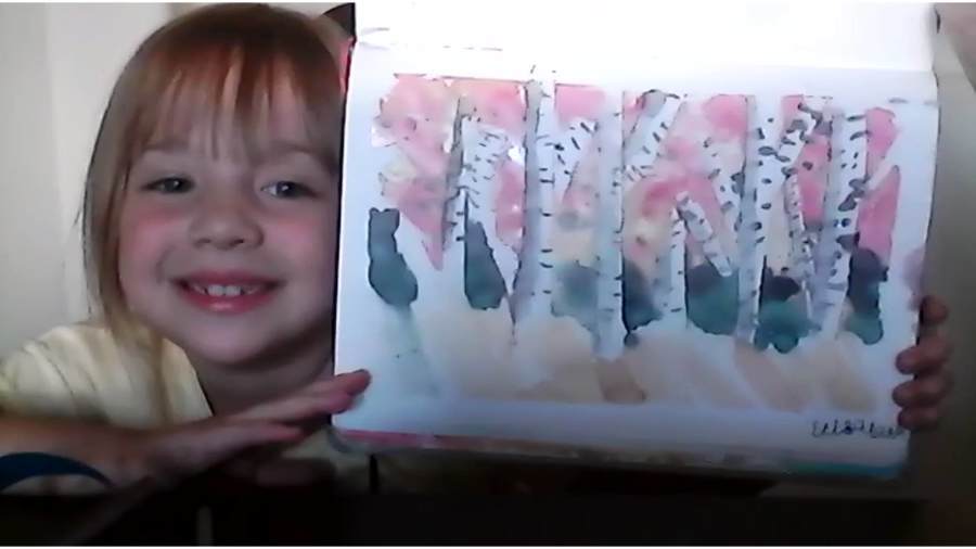 Child smiling and holding a colorful painting with abstract designs.