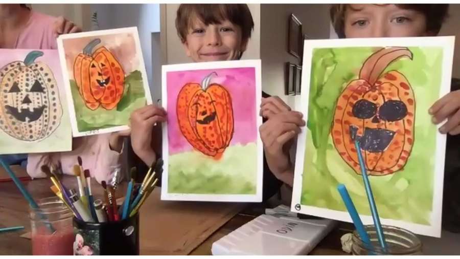 Children showing their painted pumpkin artwork at a table with art supplies.