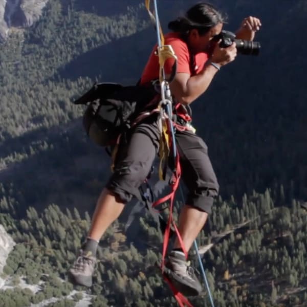 Jimmy Chin hanging off the side of a cliff with a camera in hand