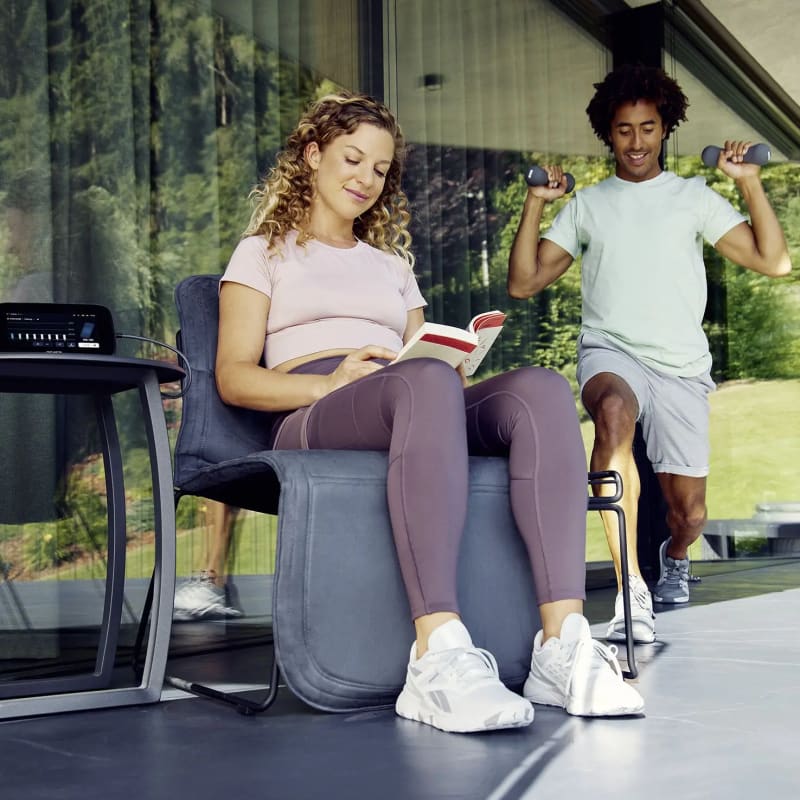 A woman using the B.Body Evo while reading a book during a break from working out