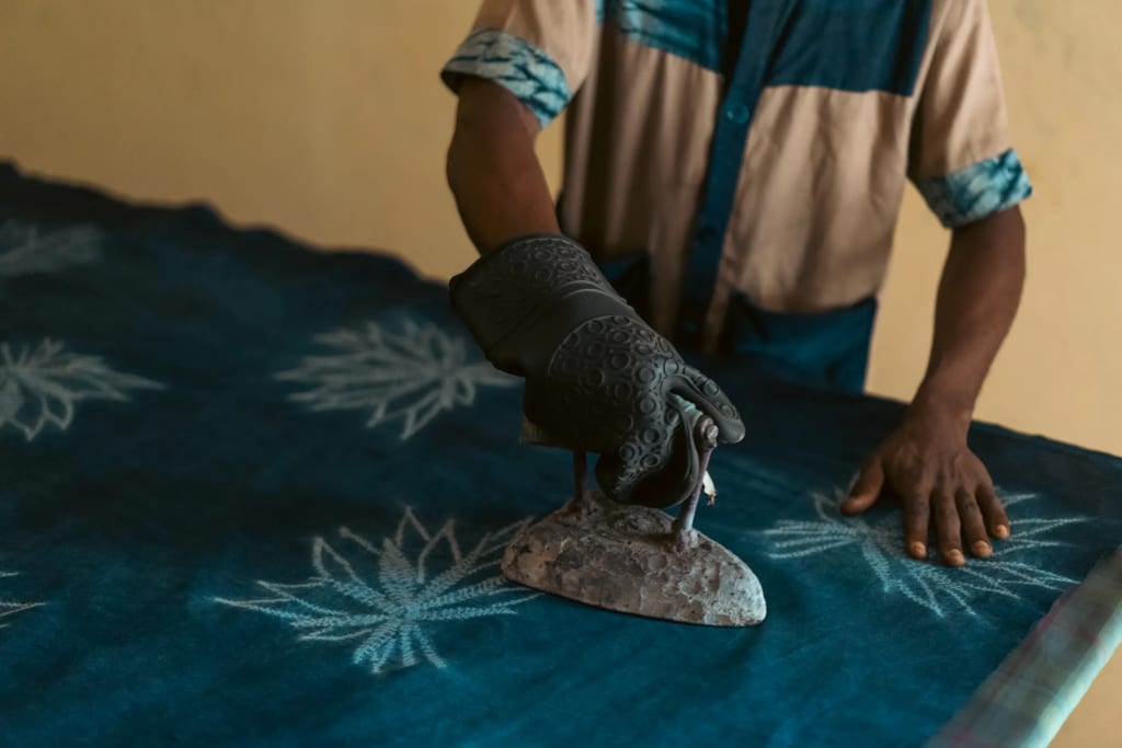 Un artisan passe un fer ancien sur un grand tissu bleu indigo orné de motifs blancs en forme de feuilles