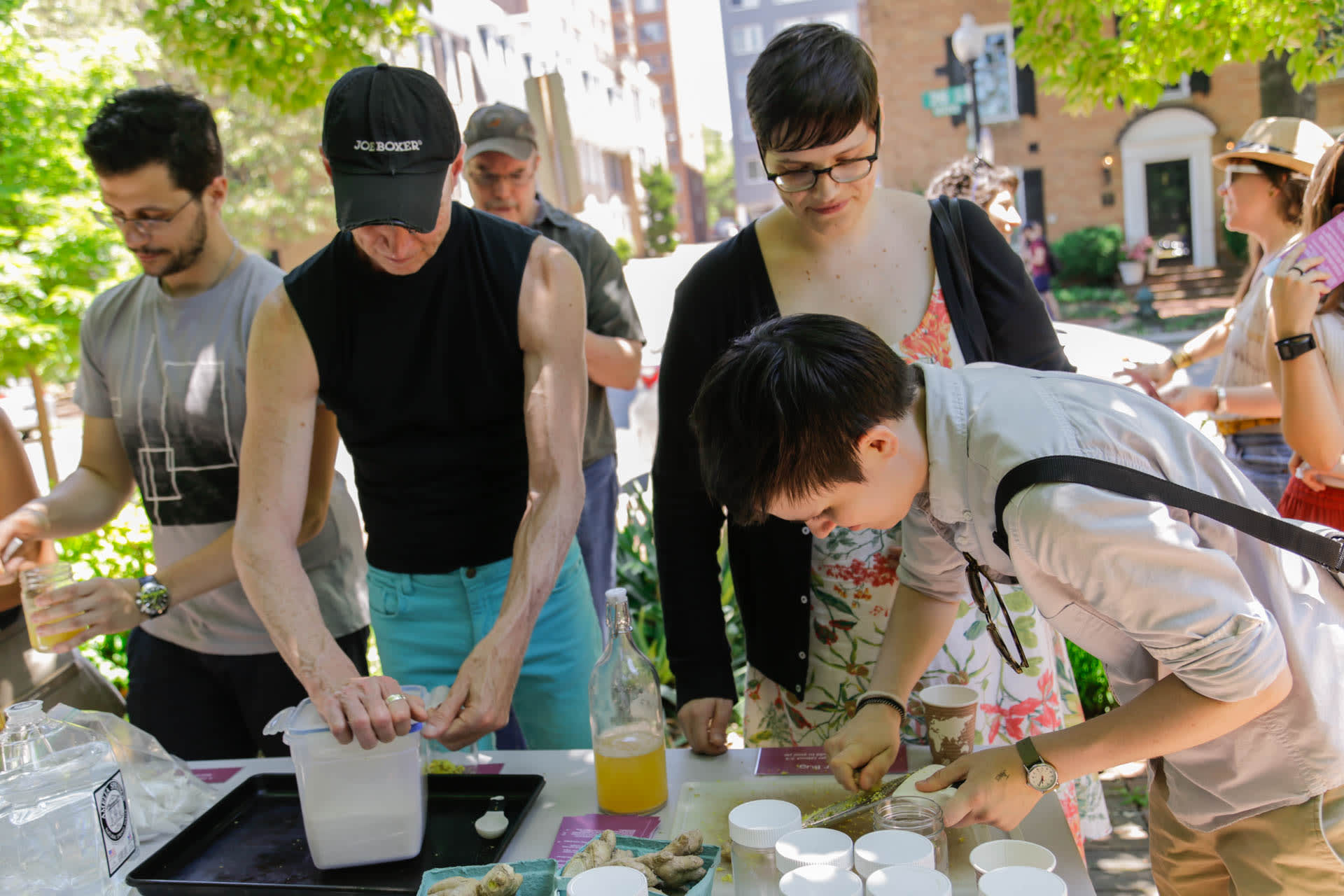 A group of people mixing ingredients at a table outdoors in a park.