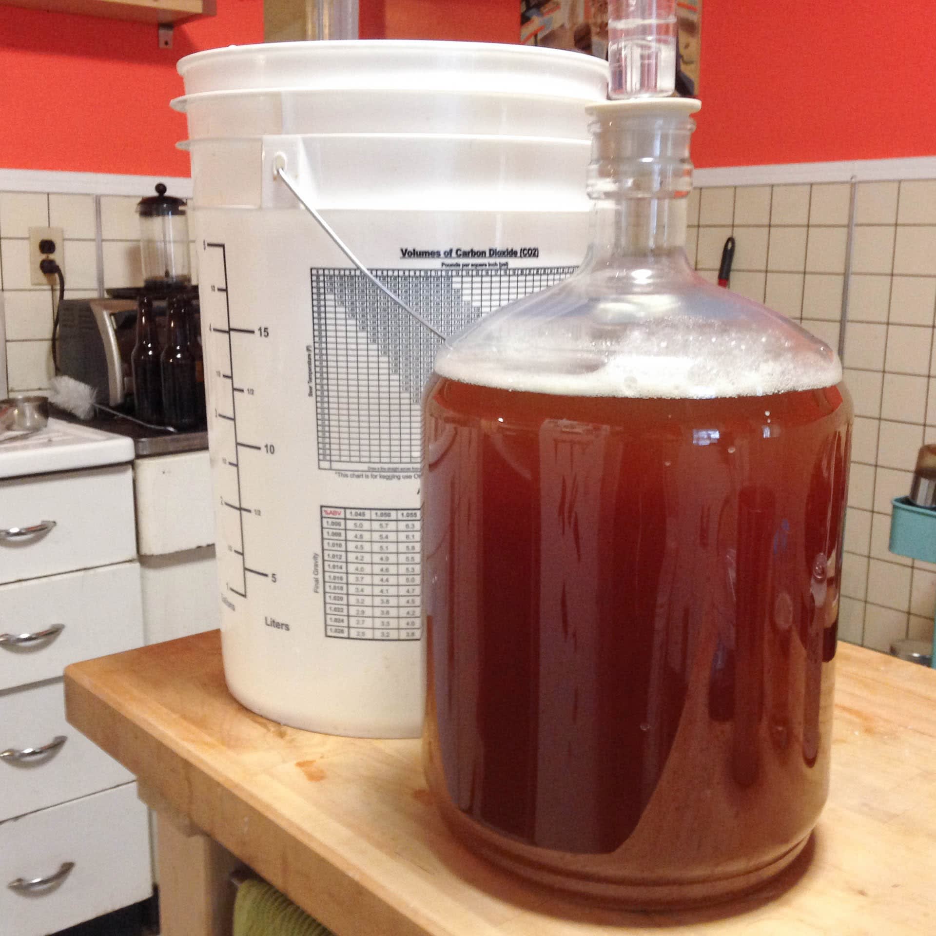 A large glass fermentation vessel, and a plastic bucket.