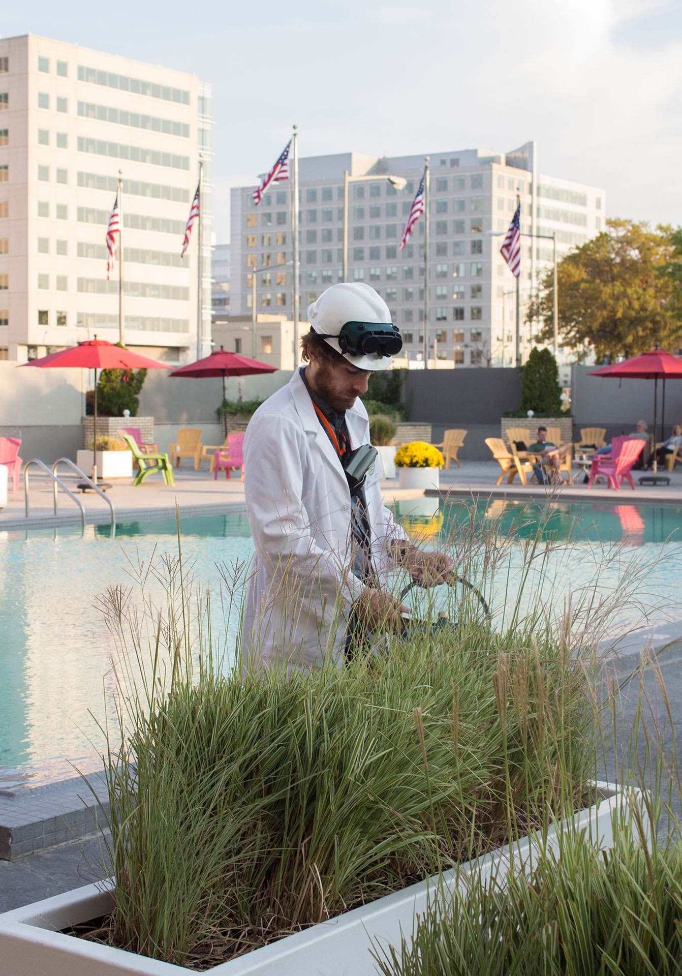 a man in a lab coat collecting grass by a hotel swimming pool