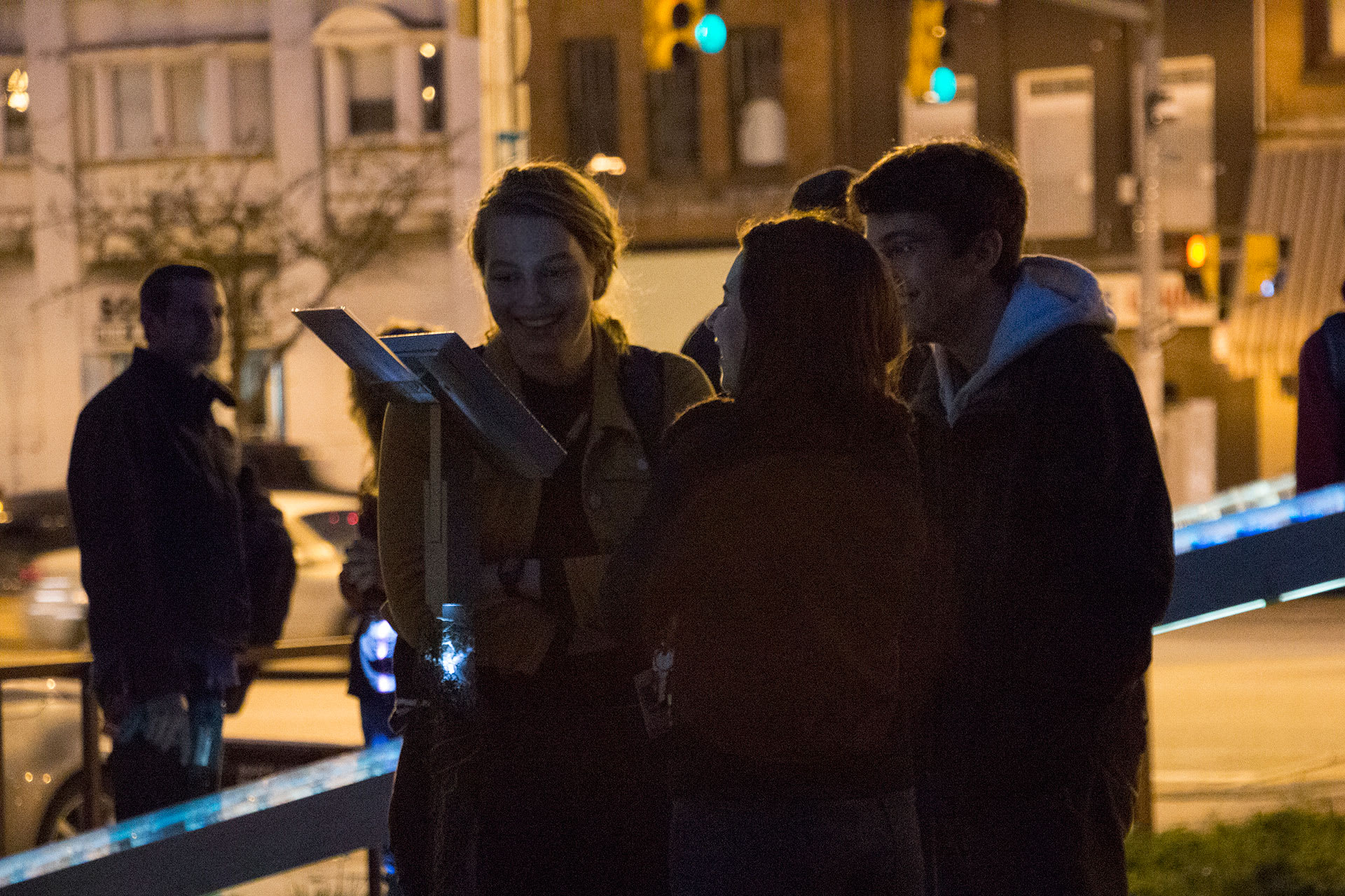 A group of young people watching a video on a tablet in a park at night