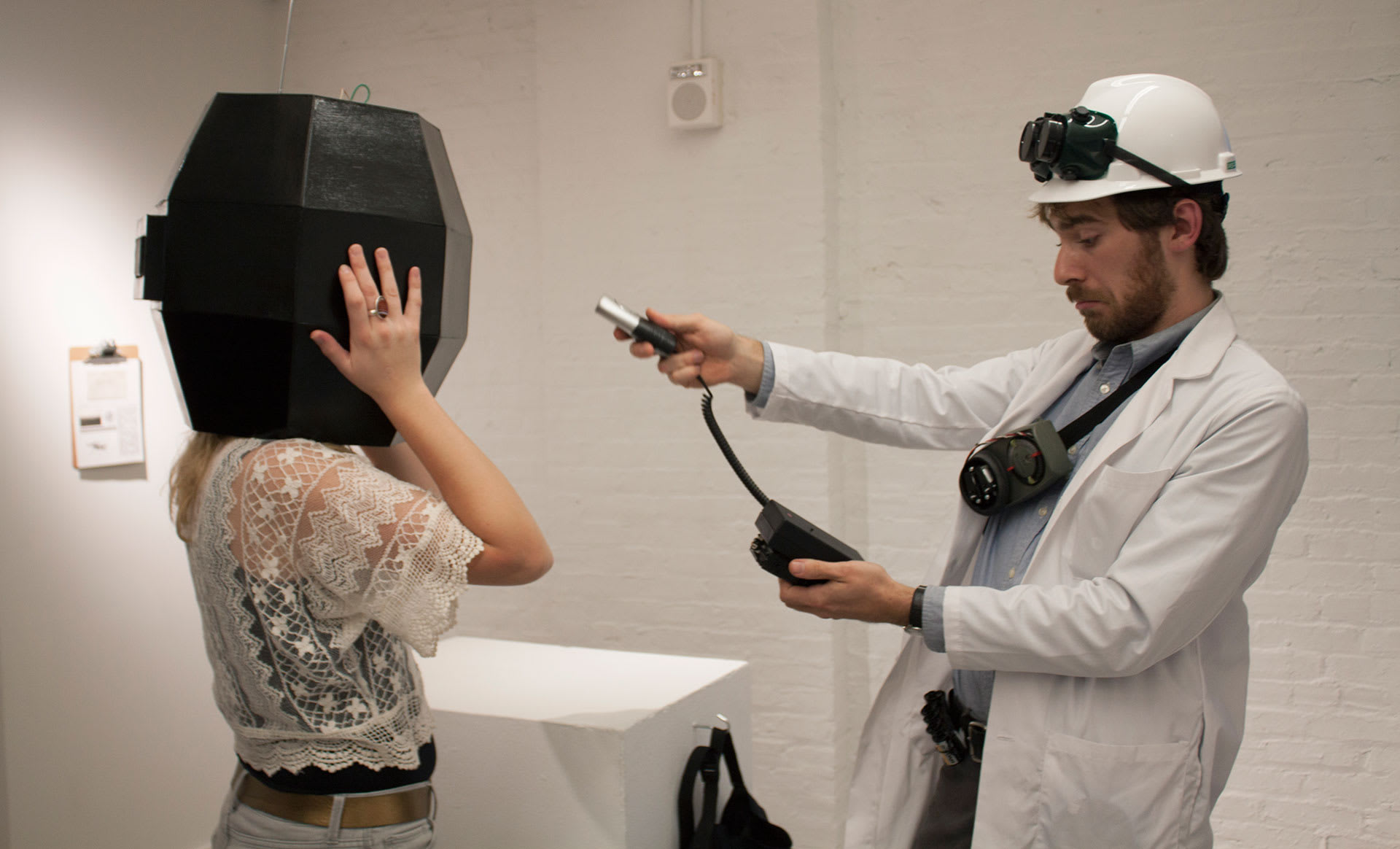 A man in a white lab coat pointing a corded device at a woman wearing a black helmet