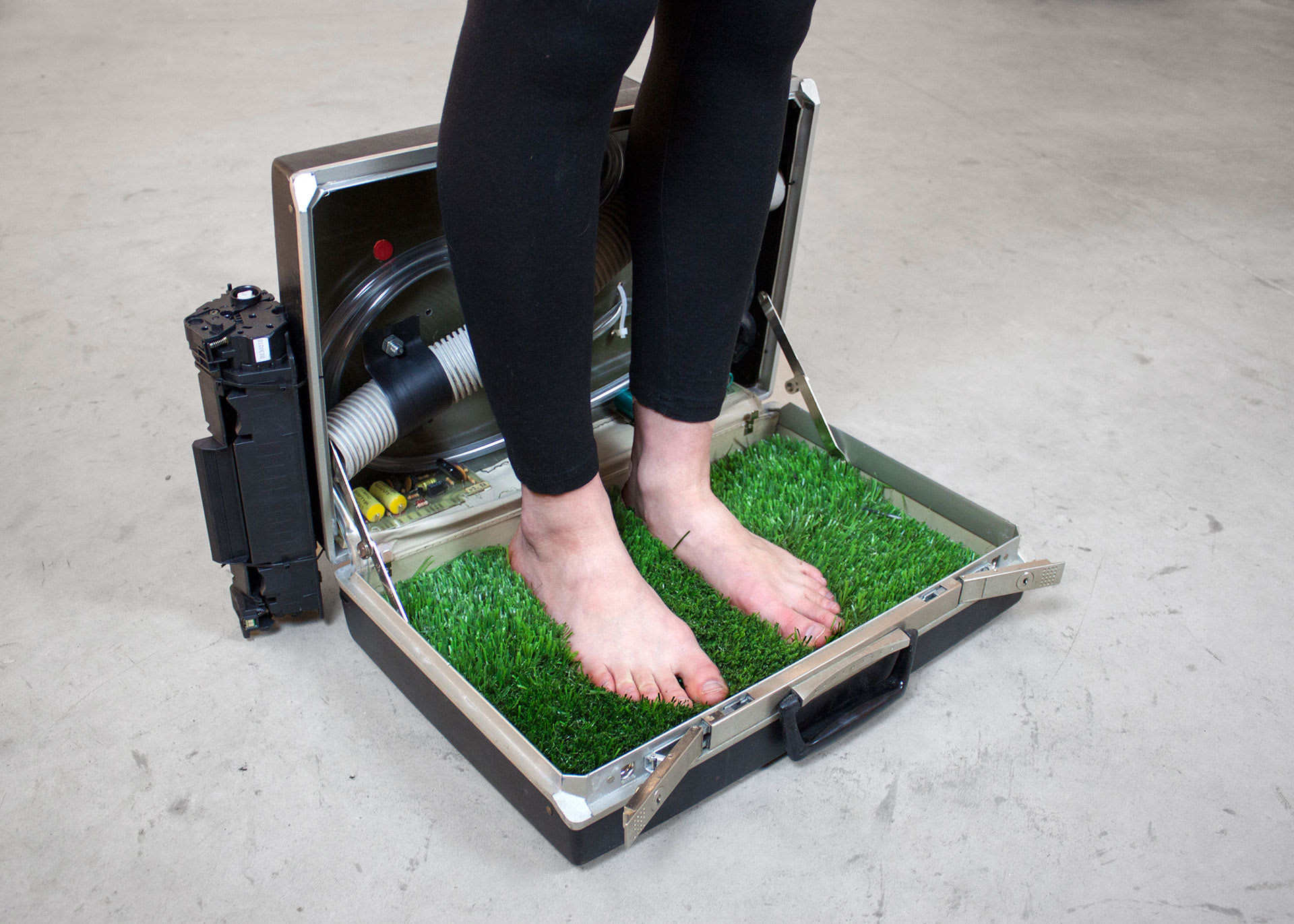 Photo of a briefcase with grass inside a womans feet standing on the grass.