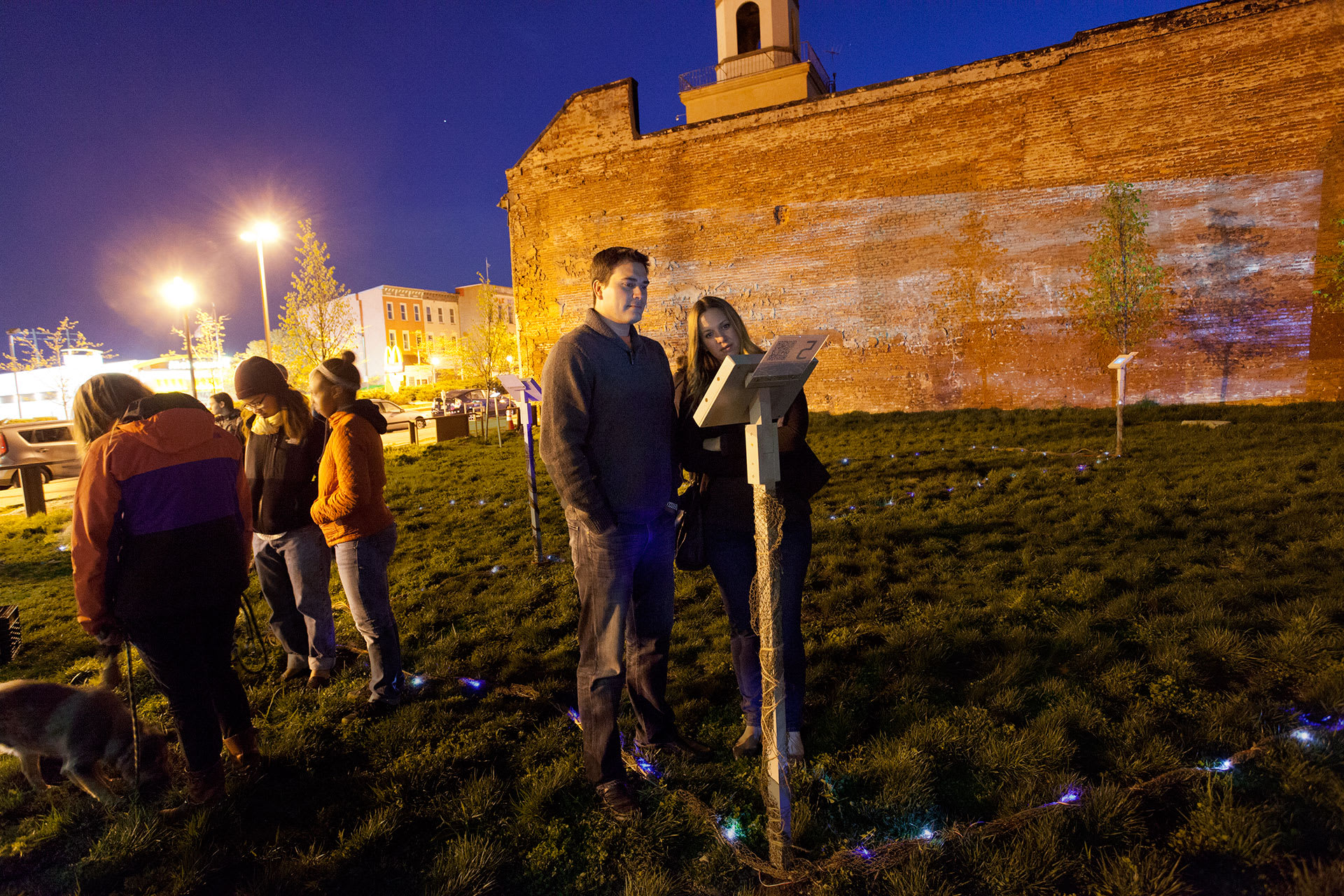 A group of young people watching a video on a tablet in a park at night