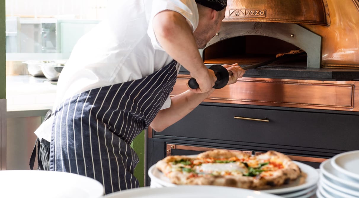 A chef putting in pizza into a pizza oven