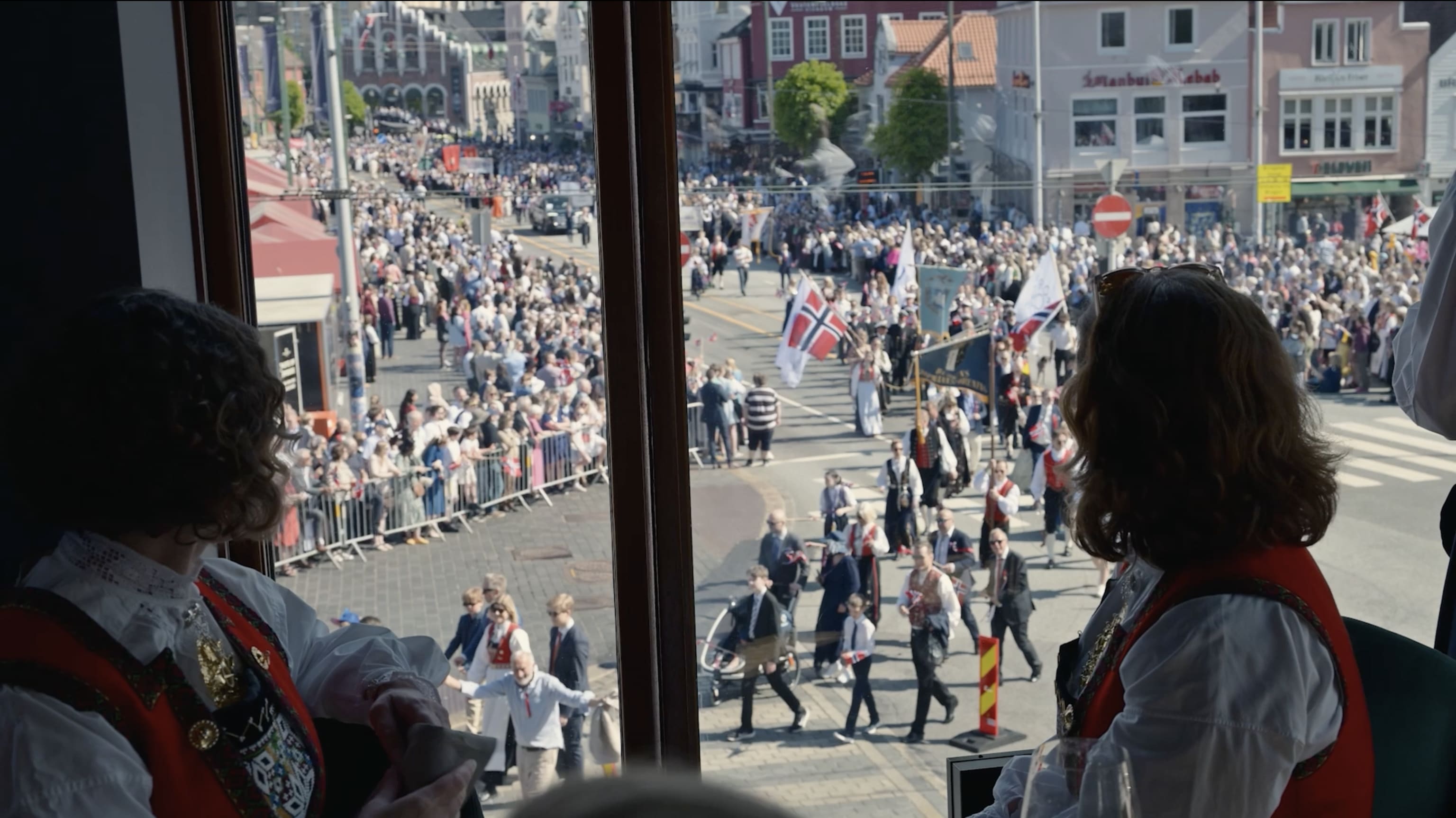 to damer som ser på 17.mai-toget fra vinduet på Bjerck med bunad