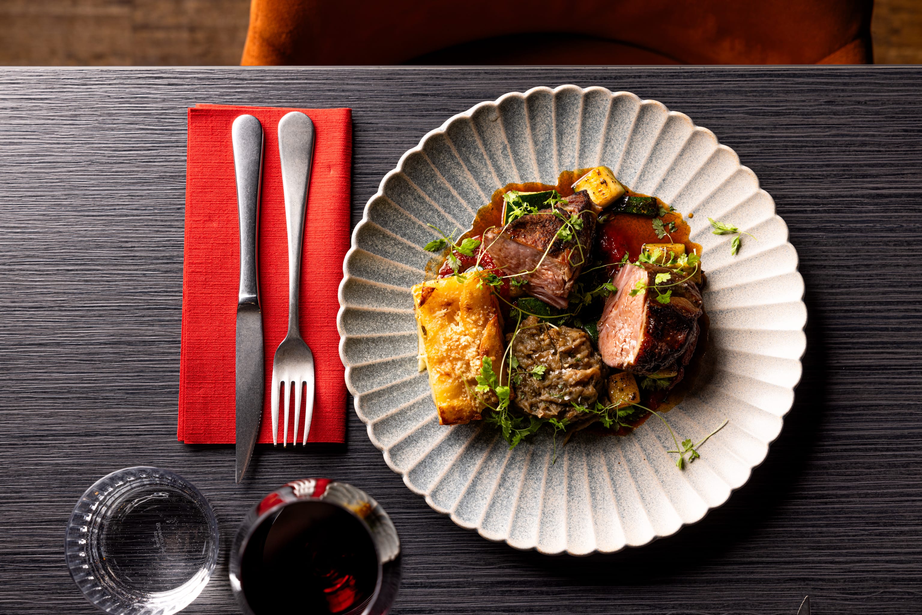 Middagstallerken på Bjerck med kjøtt, grønnsaker og saus ved siden av en rød serviett og et glass rødvin.  med kjøtt, grønnsaker og saus ved siden av en rød serviett og et glass rødvin.