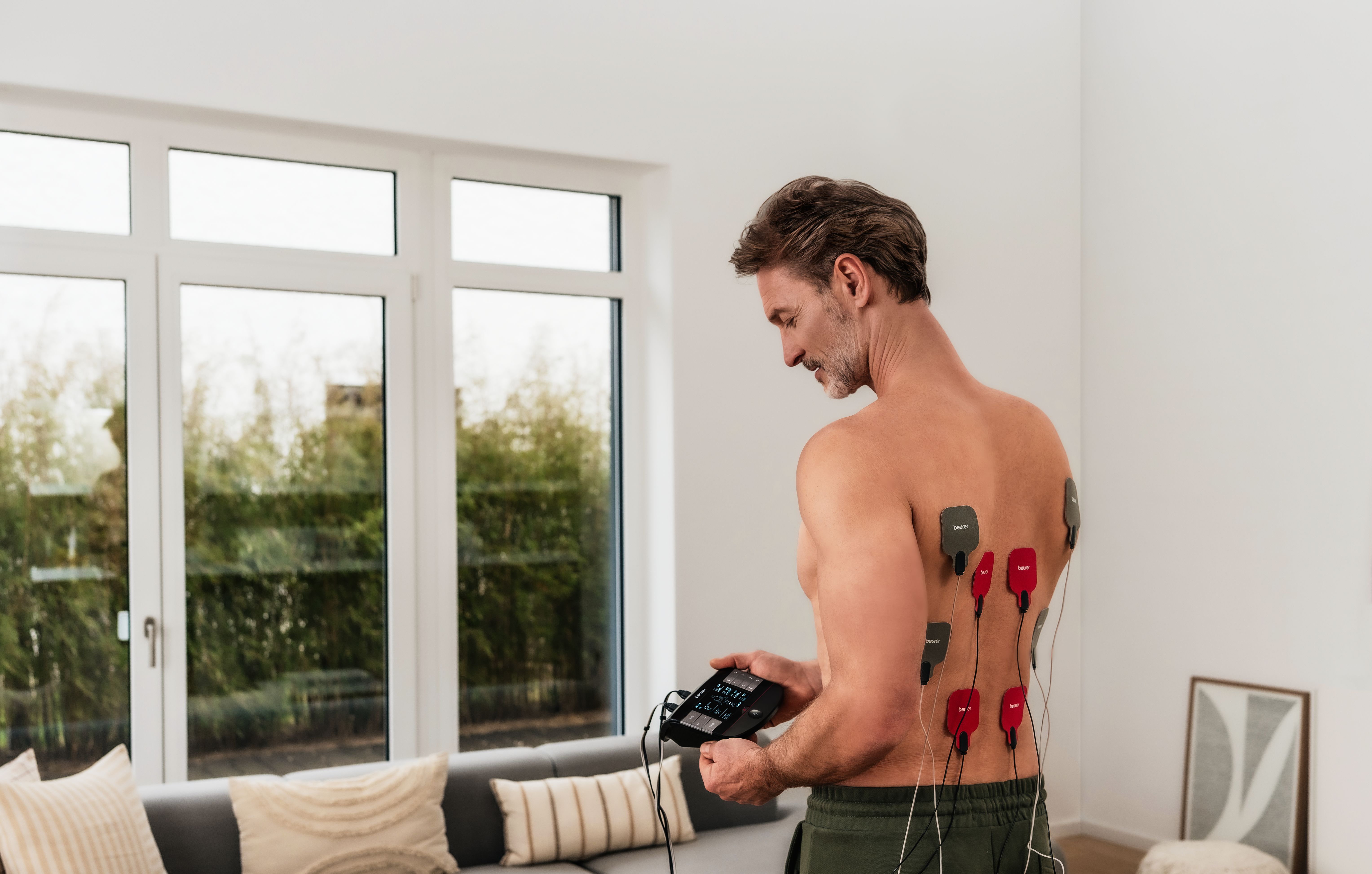 Mann benutzt EM 59 TENS Gerät von Beurer im Wohnzimmer