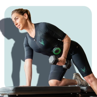 Una mujer bien entrenada hace un ejercicio con mancuernas en un banco. Lleva el traje Antelope EMS con pantalones cortos. Una mujer bien entrenada hace un ejercicio con mancuernas en un banco. Lleva el traje Antelope EMS con pantalones cortos.