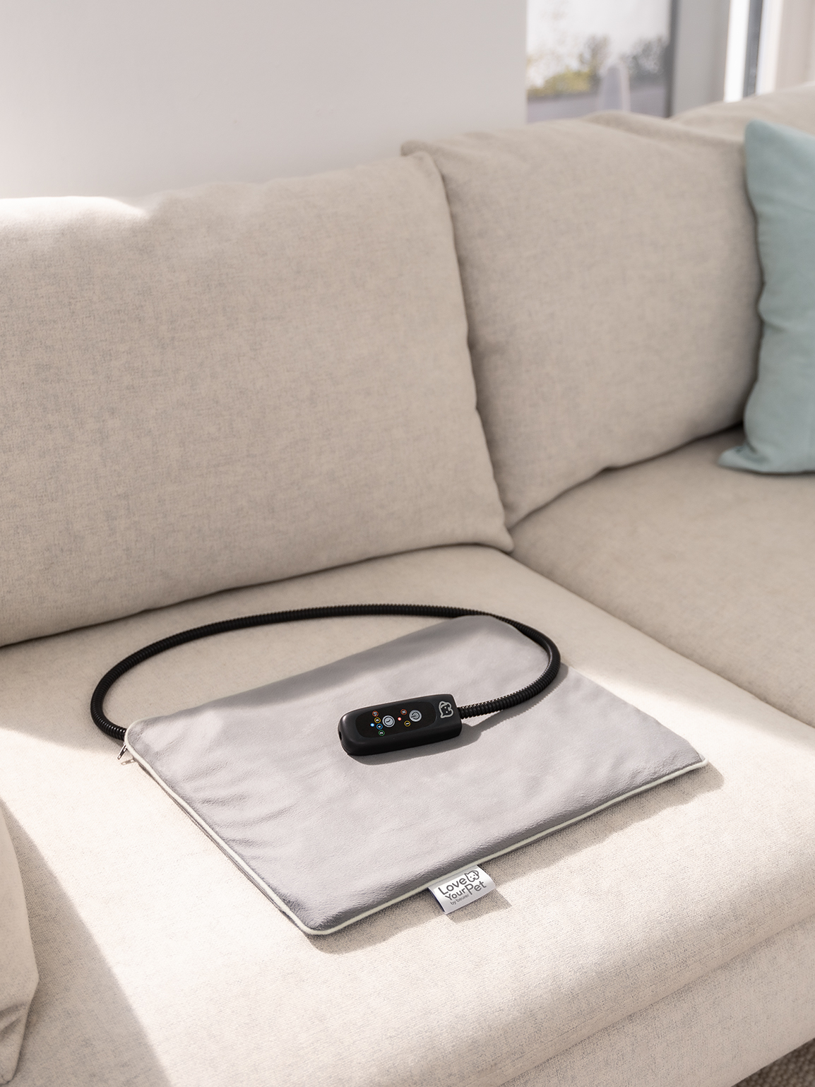 Graues Beurer-Wärmekissen aus der PetCare Serie liegt auf einem hellen Sofa.