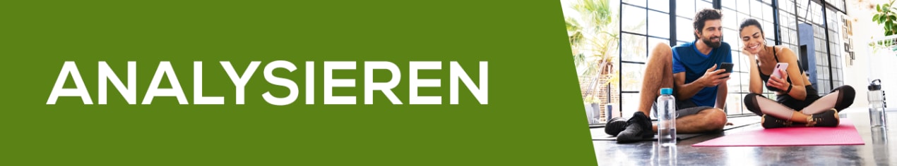 Zwei Personen sitzen auf einer Fitnessmatte und schauen gemeinsam auf ein Smartphone, um ihre Trainingsergebnisse zu analysieren – im Bild ist der Schriftzug ‚Analysieren‘ zu sehen.