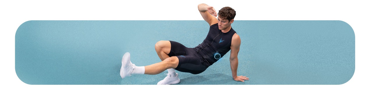 Ein sportlicher junger Mann trainiert auf einem Sporthallenboden mit dem EMS Tank-Top von Antelope.