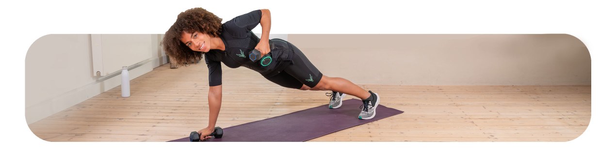Una joven entrena en casa en el suelo con pesas. Realiza una flexión lateral y lleva puesto el traje EMS de Antelope.