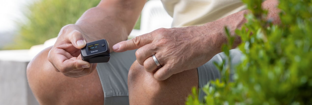 Mobile Messung: Ein Mann sitzt entspannt draußen und hält ein kompaktes Beurer Pulsoximeter bereit, um seinen Sauerstoffgehalt zu messen.