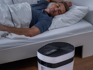 Mann liegt bei Dämmerung im Bett und schläft und daneben steht auf dem Boden das Beurer maremed Meeresklimagerät