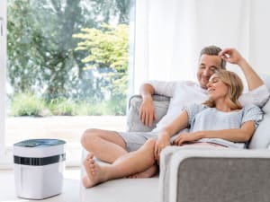 Ein Mann und eine Frau liegen gemütlich auf dem Sofa und daneben steht das Beurer maremed Meeresklimagerät