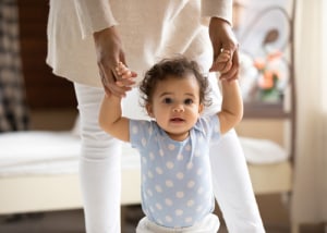 Baby läuft an den Händen ihrer Mutter