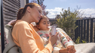 A mother is holding her daughter in her arms; the girl is using a Beurer inhaler with her eyes closed