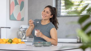 A young woman is standing in the kitchen, smiling as she holds a healthy meal in her hand