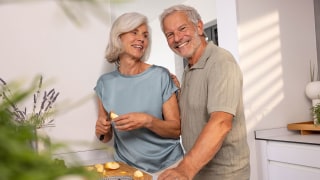 An elderly couple are standing together in the kitchen, preparing a healthy meal