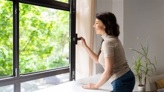 Lächelnde Frau öffnet ein Fenster in ihrem Zuhause