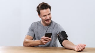 Mann misst Blutdruck mit BM 81 easyLock sitzend am Tisch über die App beurer Healthmanager Pro 