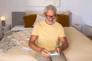 Mann sitzt auf dem Bett und nutzt das Mobile EKG-Gerät ME 95