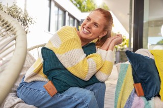 Eine Frau sitzt auf einem Sofa und hat ein Beurer HK 77 Heaty Heizkissen unter den Armen.
