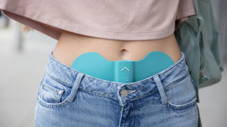 Frau trägt das Beurer EM 55 Menstruations-Pad am Unterbauch gegen Regelschmerzen, unterwegs im Freien.