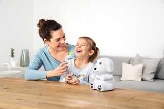 Eine Mutter hält ihrer lachenden Tochter die Inhalationsmaske des Beurer IH 24 Kids an den Mund.