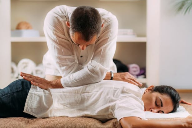 Therapeut führt Shiatsu Massage bei bekleideter Frau durch Therapeut gibt einer bekleideten Frau eine Shiatsu-Massage und übt mit seinem Körpergewicht gezielt Druck auf ihren Rücken aus