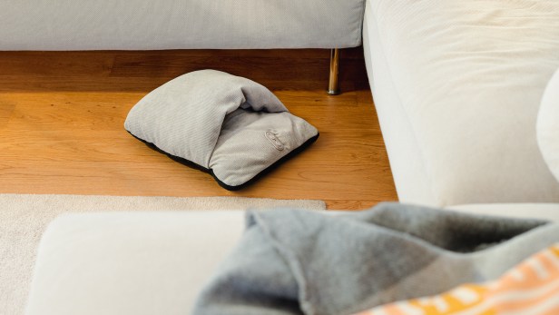 Der Fußwärmer FM 28 von Beurer liegt auf braunem Paket neben einem grauen Sofa