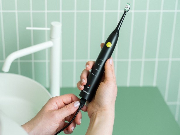 Im Badezimmer: Person hält die SC 30 in einer Hand und steckt das USB-C-Ladekabel mit der anderen Hand in die Schallzahnbürste