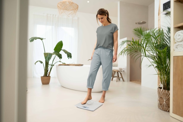 Vrouw weegt zich met de multifunctionele weegschaal "Polly" in de badkamer