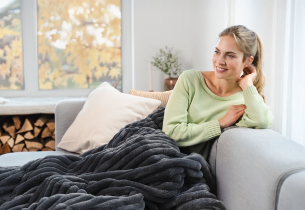 Mann sitzt am Tisch, misst Blutdruck mit Oberarmmessgerät und blickt lächelnd auf sein Smartphone.
