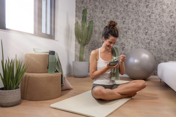 Une femme est assise sur un tapis de yoga et savoure son muesli sain.