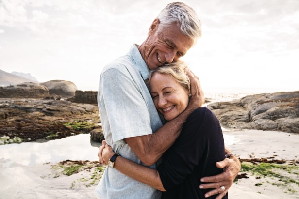 Älteres Paar umarmt sich am Strand Älteres Paar umarmt sich und lächelt, im Hintergrund ist ein Strand