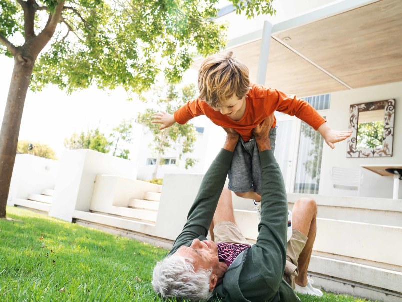 Mężczyzna bawi się z dzieckiem w ogrodzie i podnosi je do góry